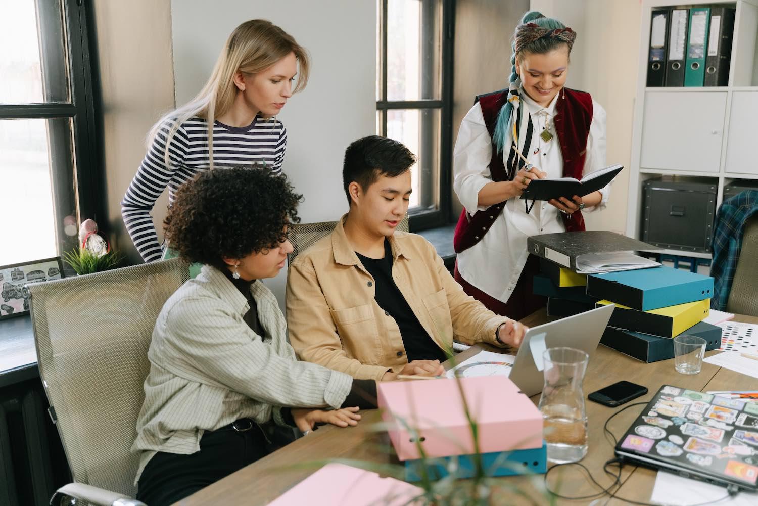 Four people working together around a laptop at an office desk
